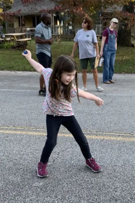 A small girl throwing a ball on the road